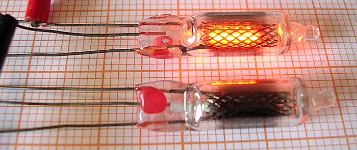 Figure 3 — 3 — Two Philips ZA1002 switching tubes on graph paper, one struck (top, glowing orange) and one dark (bottom), showing the coaxial construction that sets them apart from an indicator neon:…